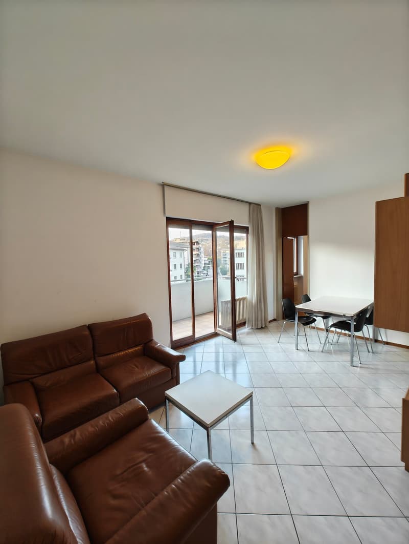 white tile floor, brown leather couches, white coffee table, white dining table, black chairs, balcony with sliding glass doors