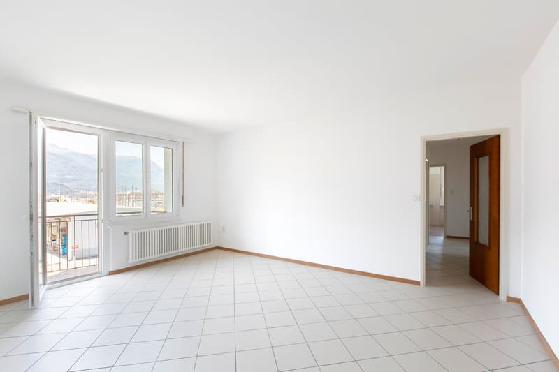 Spacious living room with large windows, tiled flooring, and a balcony or terrace overlooking the city