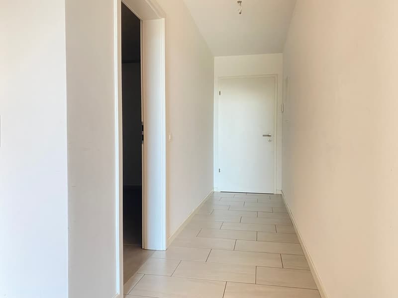 corridor with white tiled flooring, white walls, white door, open door leading to another room, light fixture on the ceiling
