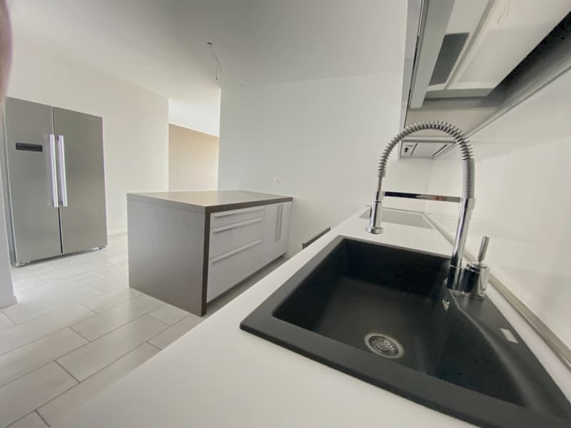 modern kitchen with black countertop, stainless steel sink and faucet, white cabinets, tiled floor, and a refrigerator