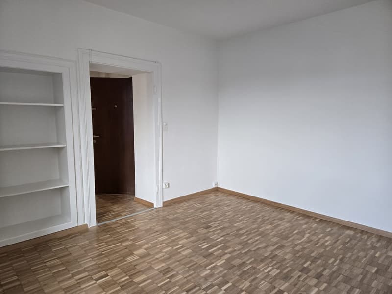 empty room with white walls, wooden parquet flooring, door, white built-in shelves