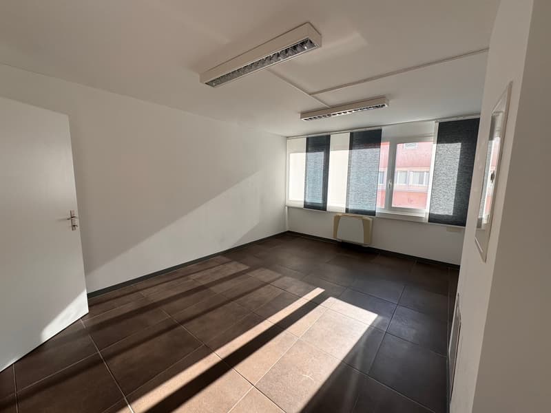 empty room with white walls, brown tiles, large window with black blinds, and white door