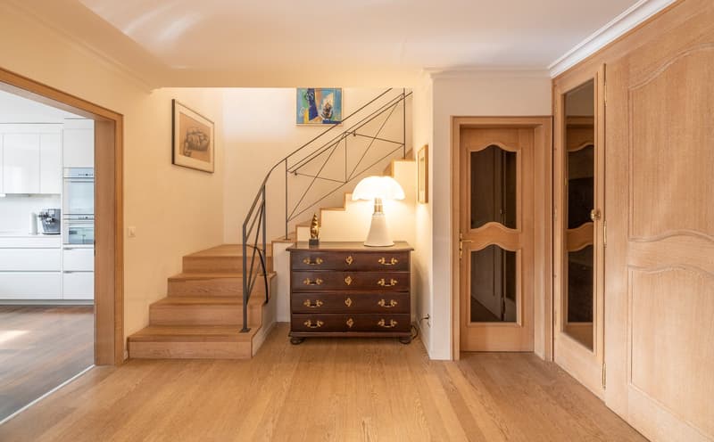 A hallway with wooden floors, a lamp, a drawer, and a painting on the wall.