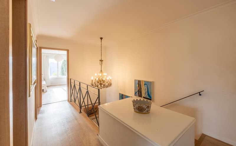 A hallway with a chandelier, a white cabinet, and a staircase with a metal railing.