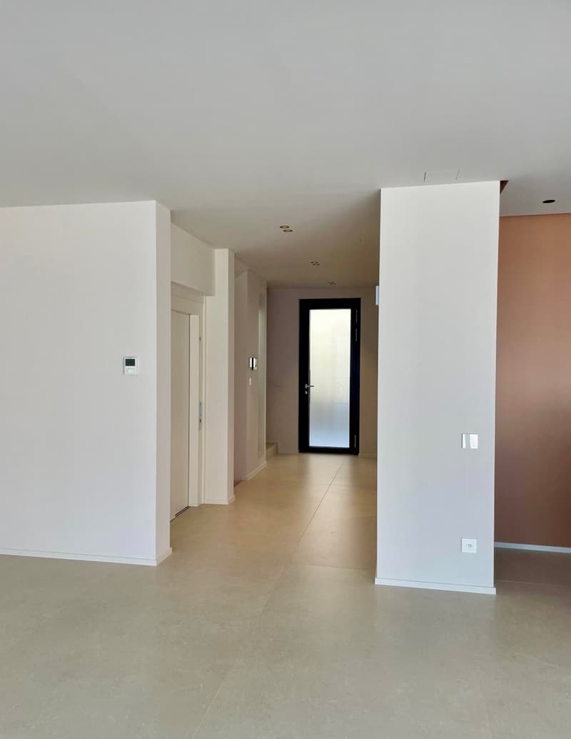 The image shows a hallway with white walls, a black door at the end, and a tiled floor. The hallway appears to be part of a larger residential or commercial space.