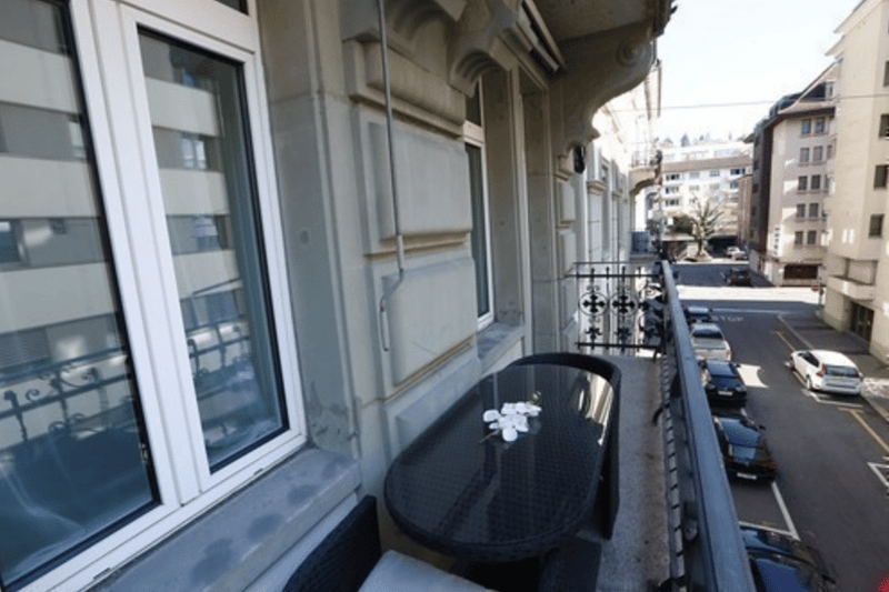 Balcony with black table and chairs, overlooking a city street with buildings and cars