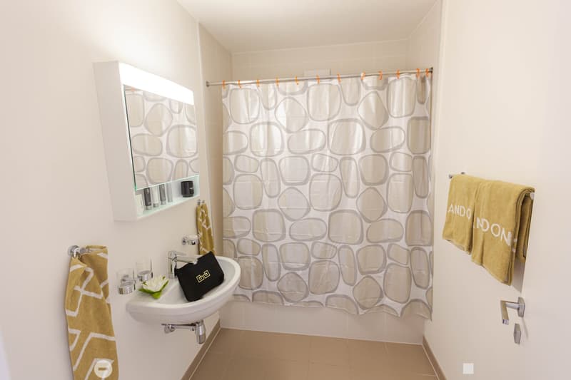 White bathroom with patterned shower curtain, white sink, mirror cabinet, and yellow towels