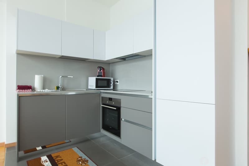Modern, minimalist kitchen with gray cabinets, stainless steel appliances including a microwave and dishwasher, and a tiled floor.