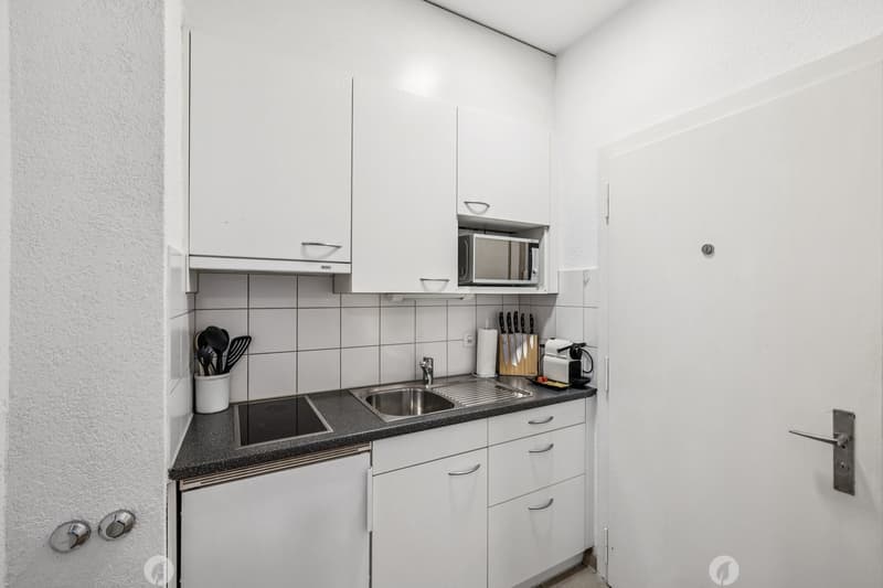 Compact kitchen with white cabinets, black countertop, sink, microwave, and kitchen utensils holder