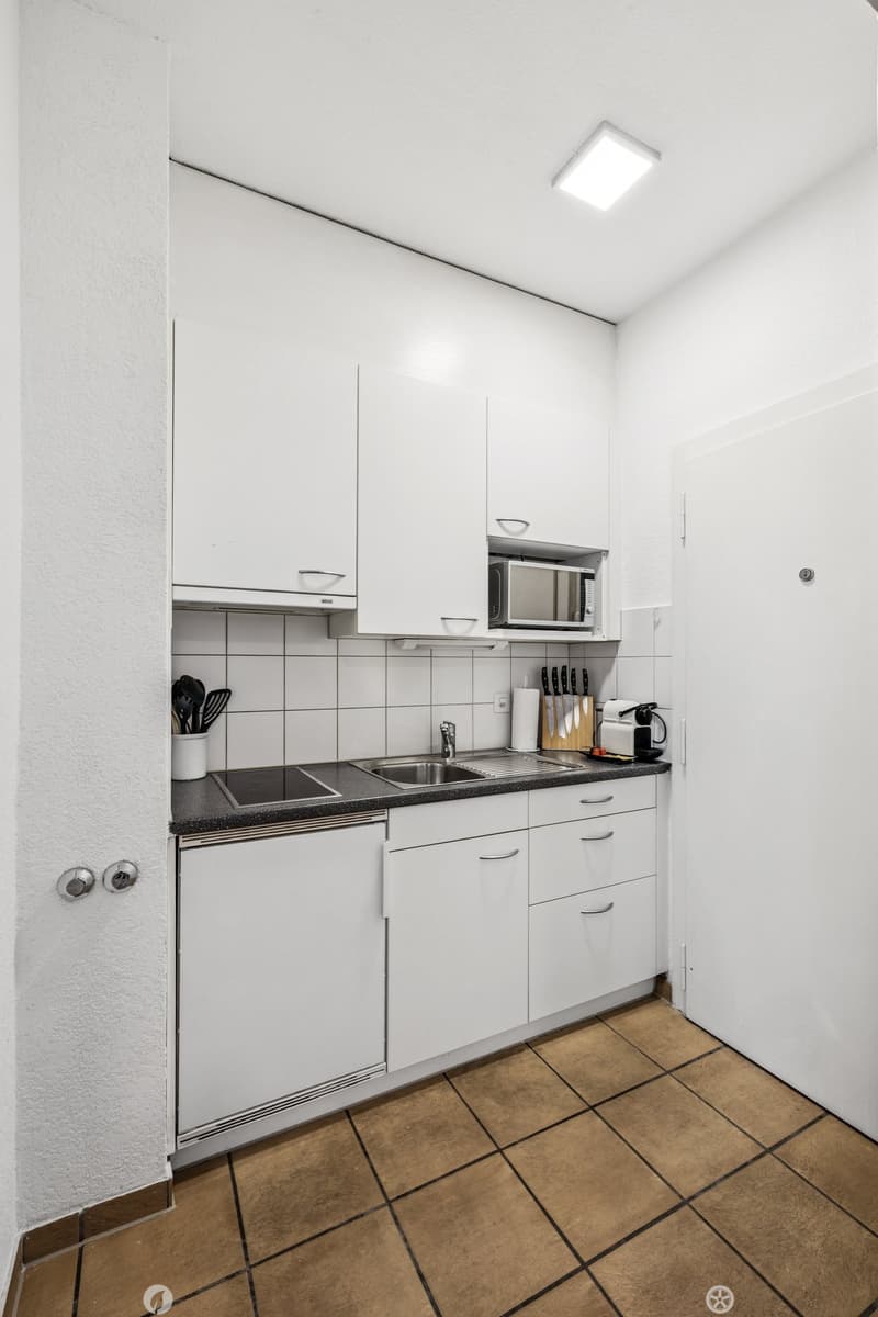 Compact kitchen with white cabinets, black countertop, tile backsplash, sink, microwave, and dishwasher