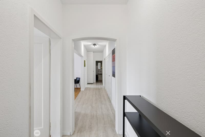 modern hallway, white walls, grey wood floor, ceiling lights, black shelf