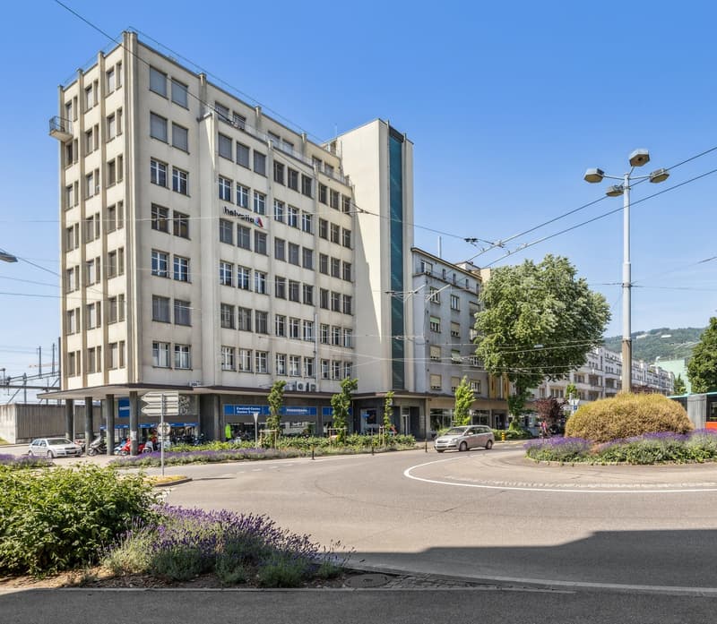 A 4-storey building with multiple windows, located on a street corner, with a small garden and street lamp.