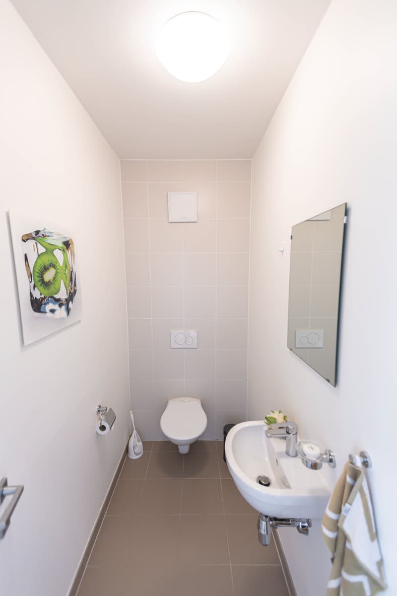 Bathroom with white walls, tiled floor, toilet, sink, and mirror. There is a framed artwork on the wall.