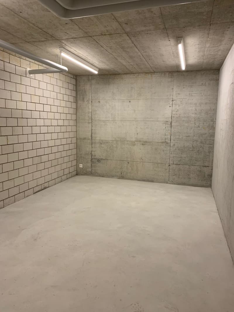 tiled wall, concrete wall, concrete floor, ceiling with mounted lights