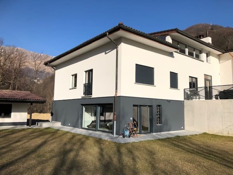 Modern two story house, white and gray walls, balcony, glass windows, located in a scenic area with mountains in the background
