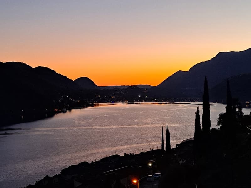 sunset over a river, surrounded by mountains, city lights visible in the distance