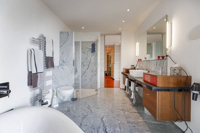 modern bathroom with a bathtub, shower, double sinks, toilet, large mirror, towel racks, wooden vanity, marble floors