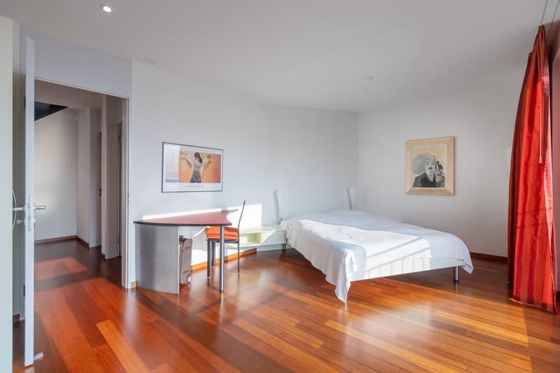 A modern room with hardwood floors, white walls, desk with chair, single bed, picture frame on wall