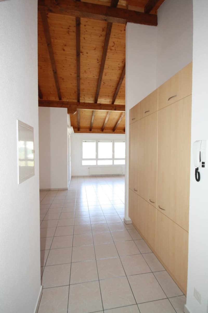Empty hallway with wooden ceiling, white tiled floor, white walls, large windows, wooden storage cabinets