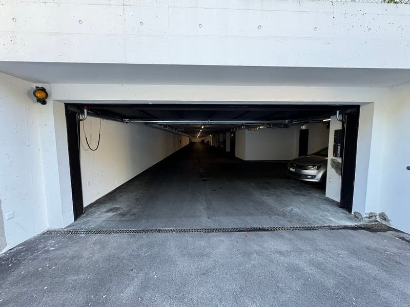 Empty underground garage with an open door, one car parked, white walls and ceiling, ceiling lights