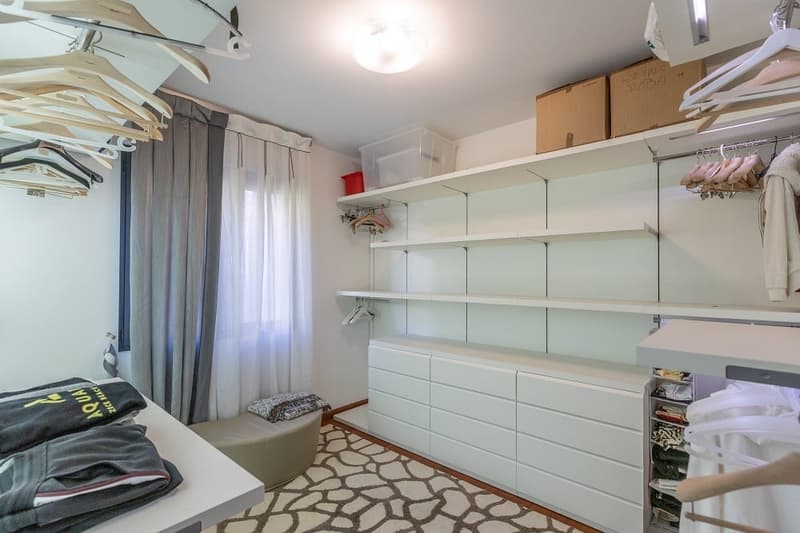 walk-in closet with white shelves, drawers, and hanging space, a table with clothes, and a bench