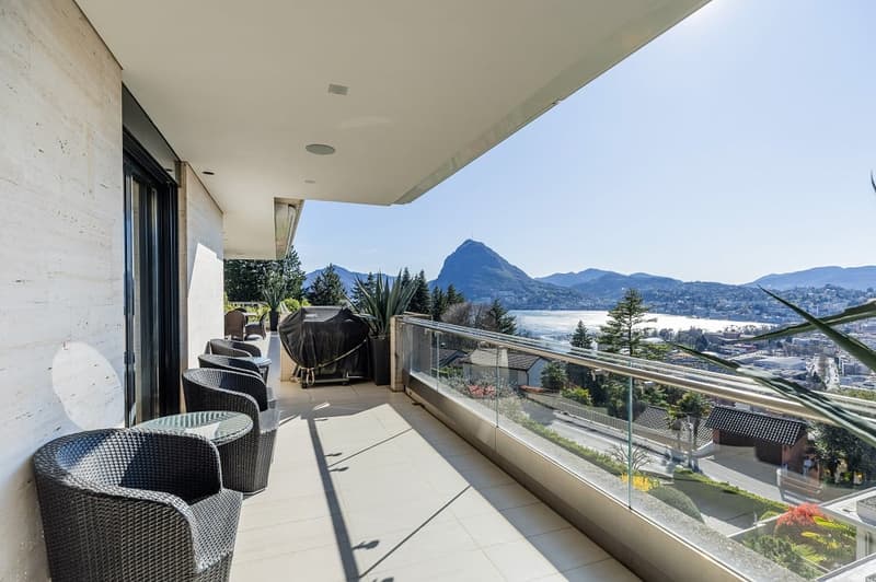 Balcony with glass railing, wicker chairs, table, plants, view of mountains and water