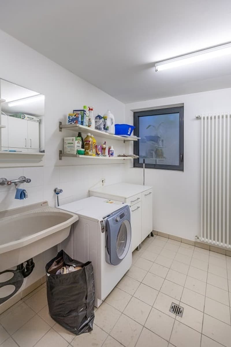 Laundry room with washing machine, sink, shelves, and radiator