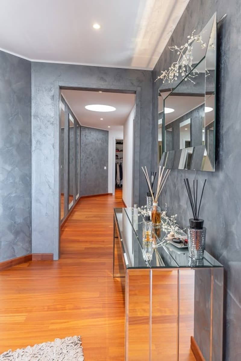 A hallway with wooden floors, gray walls, a glass table, and a mirror.