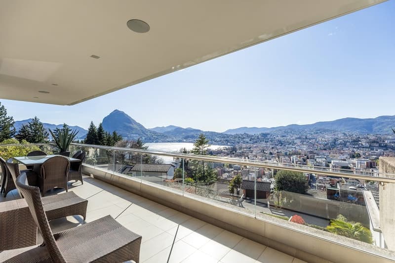 large balcony with glass railing, table and chairs, overlooking mountains and city