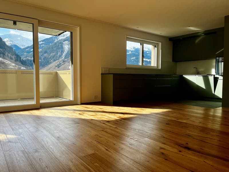 Modern kitchen with sliding glass doors leading to a balcony, wooden floors, and a scenic mountain view.