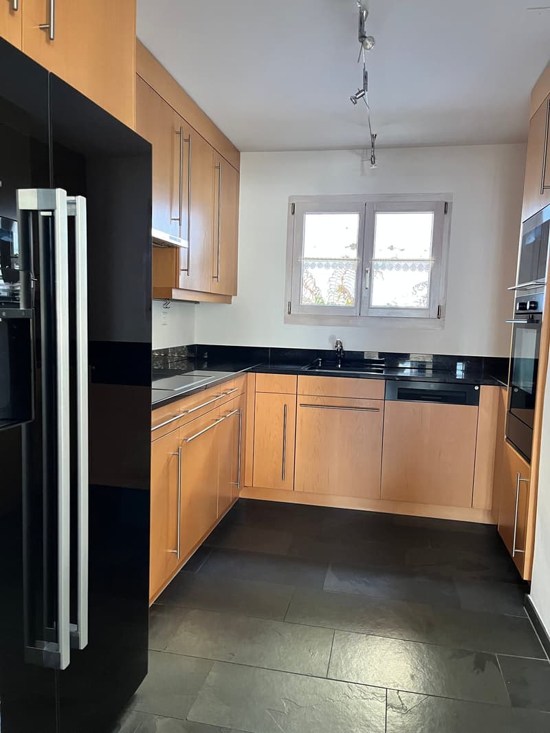 modern kitchen with dark flooring, wooden cabinets, black countertops, integrated dishwasher, black refrigerator, built-in microwave, and a window with a white frame