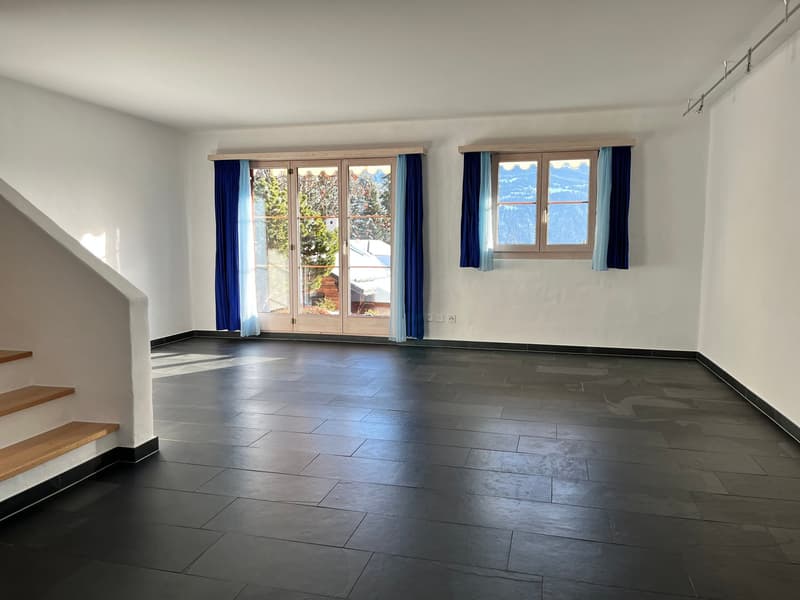 Empty room with large windows, black tiles floor, wooden stairs, two window curtains