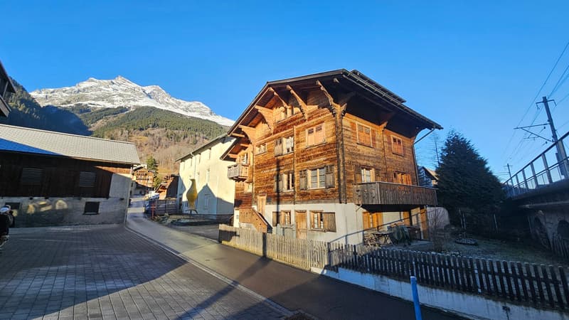 3 story wooden house, balcony, gable roof, trees in front, mountains in the background