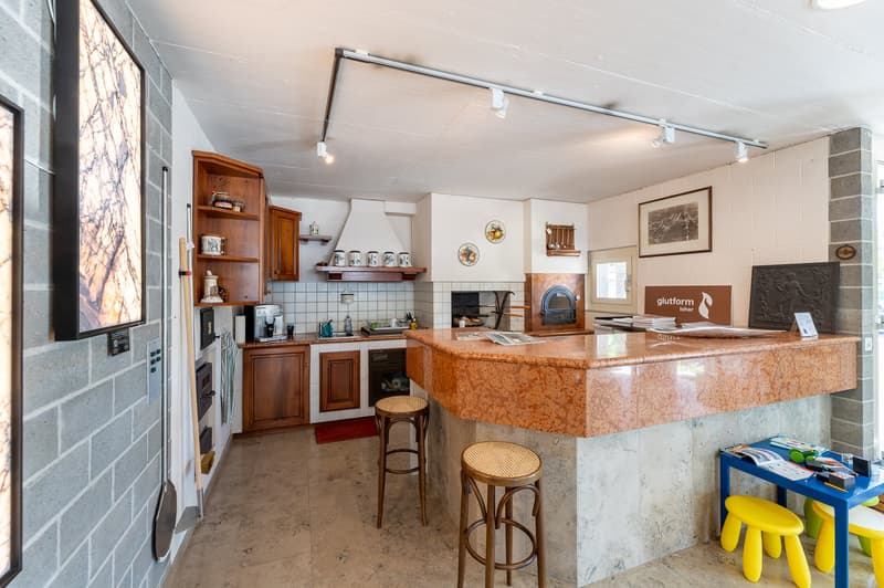 C-shaped island counter, built-in kitchen cabinets, wooden stools, large countertop, hanging kitchen utensils, tile flooring, tiled backsplash, artwork on the wall, a microwave, an oven, and a refrigerator