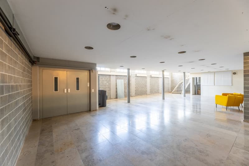 spacious and bright room, entrance door, white tile floor, staircase, white pillars, air vents, gray walls