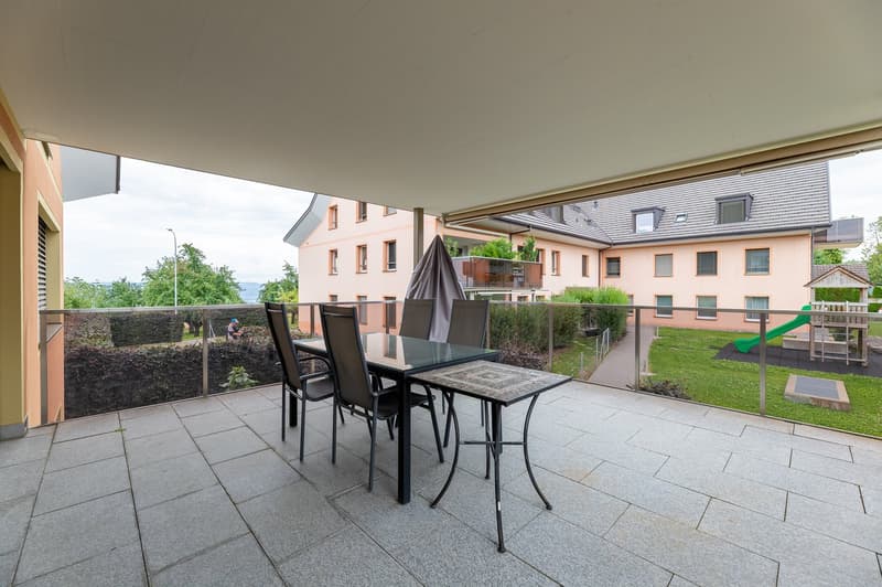 Outdoor dining table and chairs, glass railing, view of a garden and a building