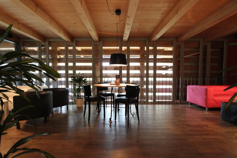 wooden ceiling, wooden floor, round table with 4 chairs, black lamp, black sofa, red sofa, plants