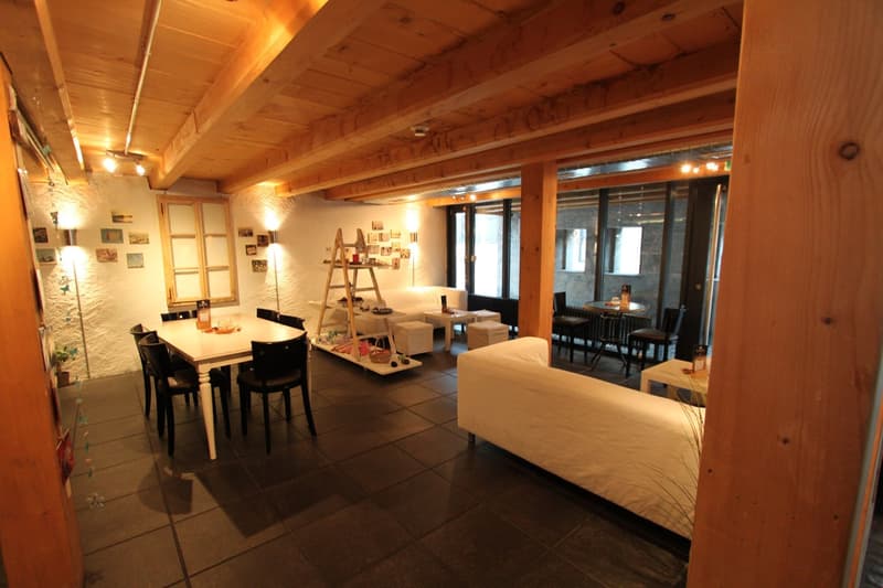 Dining room with wooden beams, white walls, black tiled floor, dining table, chairs, white couch, white side table, ladder, shelves, and lamps