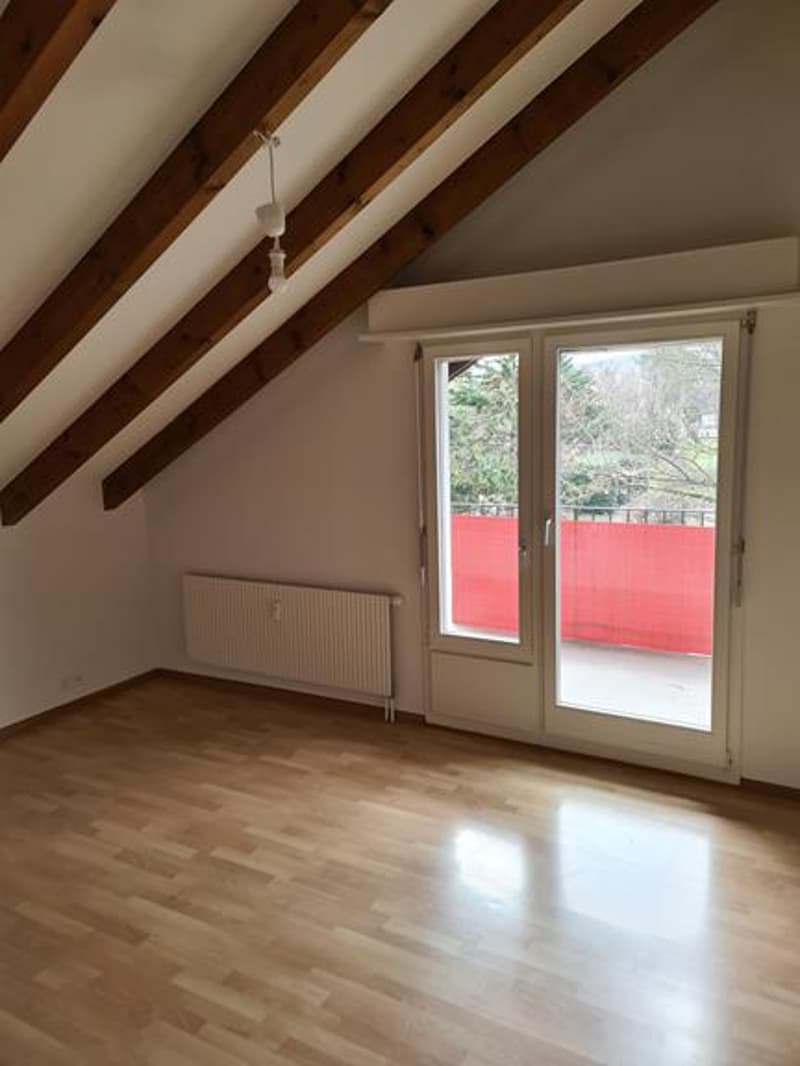 Attic room with exposed wooden beams, hardwood flooring, and a sliding glass door leading to a balcony or terrace.