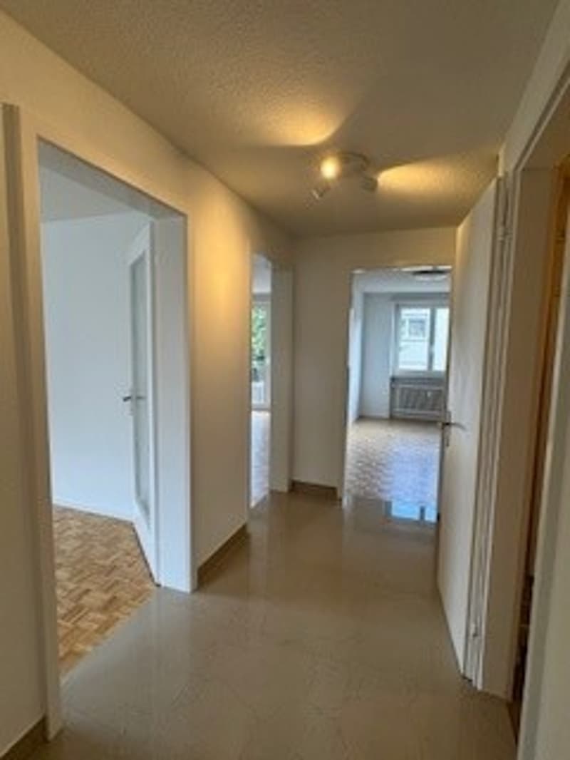an empty hallway with tiled floor and white walls, several doors on the side, and lights on the ceiling