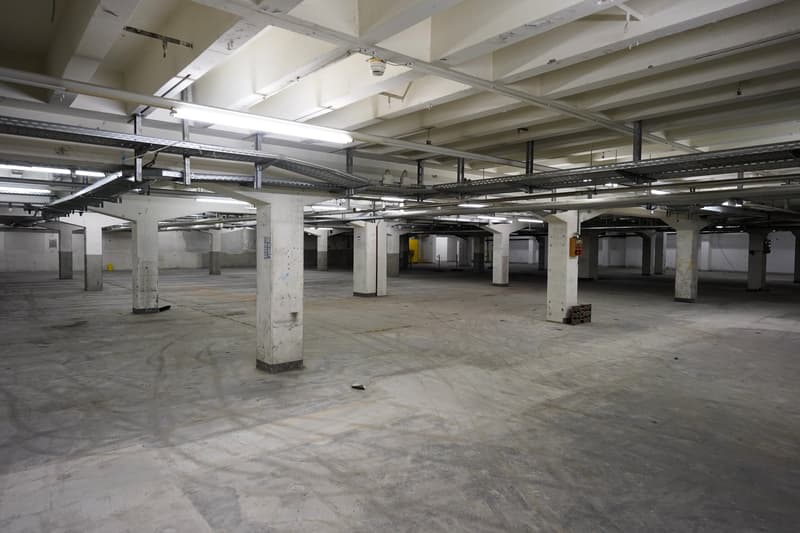 open parking area with high ceiling and white columns, concrete floor, fluorescent lighting