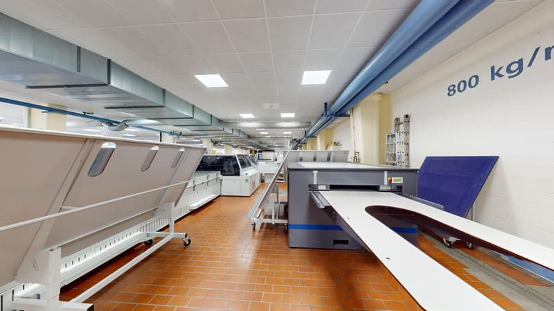 Industrial facility with brick flooring, industrial equipment on wheels, blue pipes, white walls