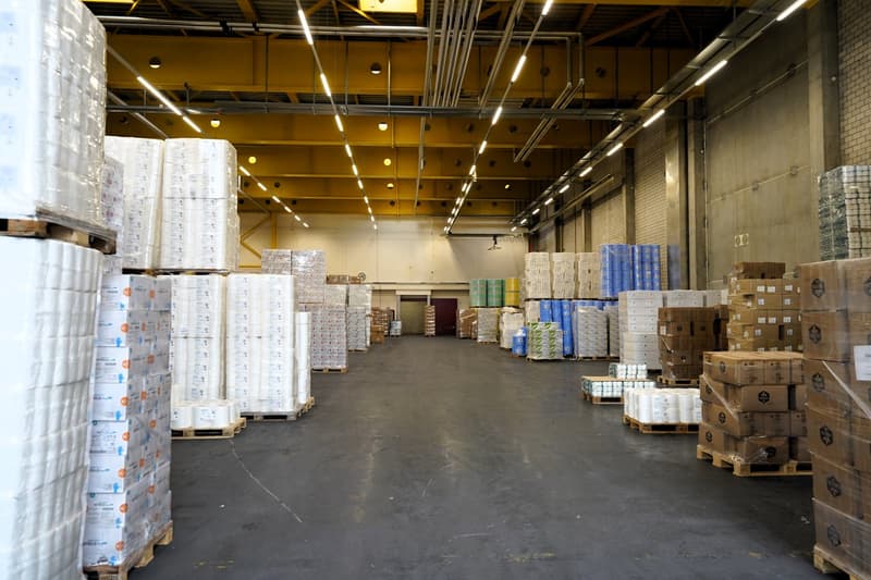 spacious warehouse with stacks of boxes and pallets, high ceiling with industrial lighting, wide open floor