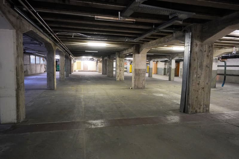 Underground parking space with concrete floor, exposed beams, and overhead lighting.