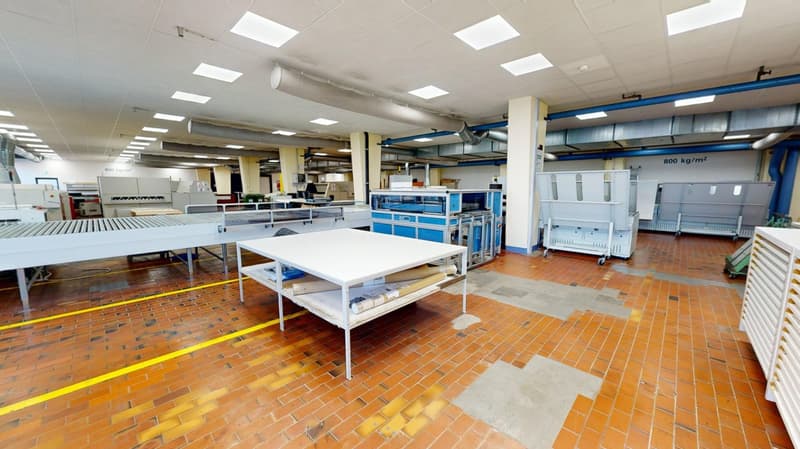 Large industrial warehouse with brick floor, multiple work stations, industrial equipment and metal storage units.
