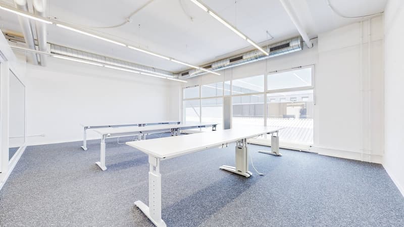 Empty room with two desks, fluorescent ceiling lights, glass windows, carpeted floor