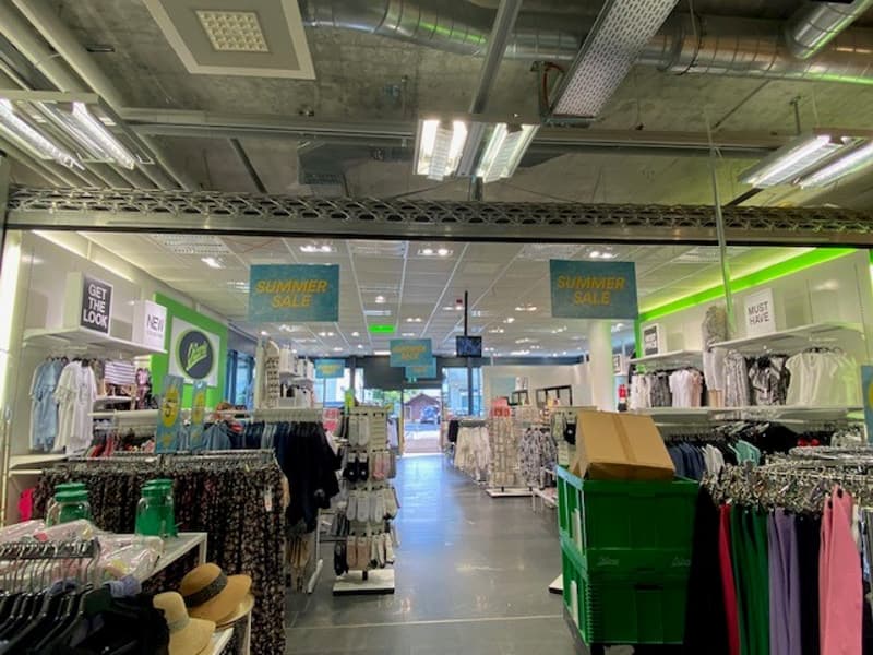Clothing store with multiple sections displaying different types of clothing and accessories on hangers, with visible lights and signage throughout the store.