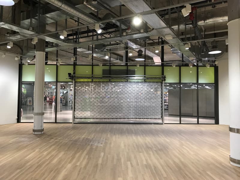 Empty room, steel sliding gate, glass walls, wooden floor, two pillars, ceiling with lamps and duct pipes