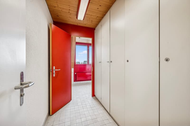 Empty hallway with tiled floor, white and red walls, and wooden ceiling.