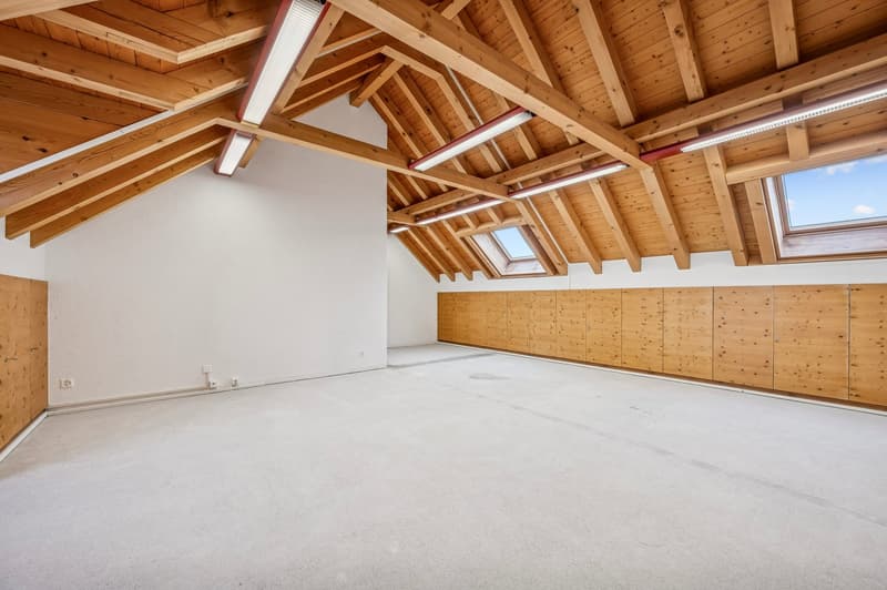 empty attic room with white walls, wooden ceiling beams, exposed wooden cabinets, white floor, skylights